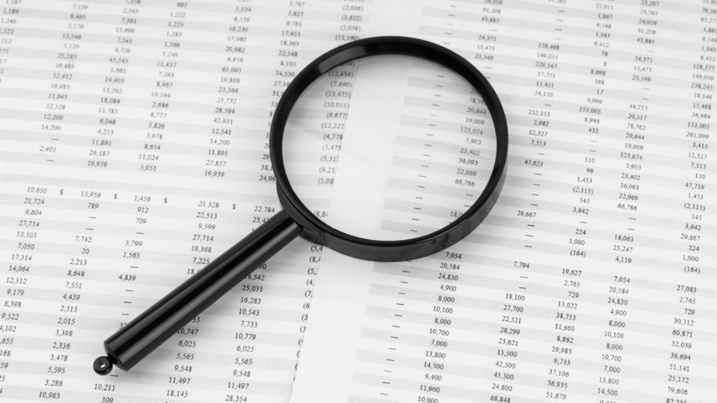 Loupe placée sur un tableau financier en noir et blanc, symbolisant l'examen détaillé des données
